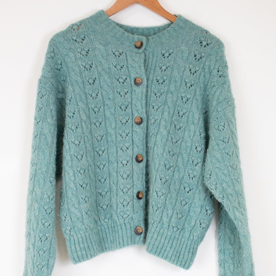 Teal knitted cardigan with wooden buttons on a hanger against a white background