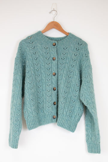 Teal knitted cardigan with wooden buttons on a hanger against a white background