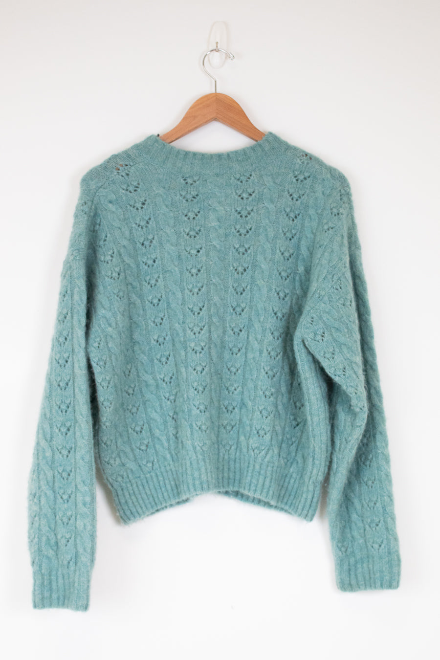 Teal sweater on a wooden hanger against a white background