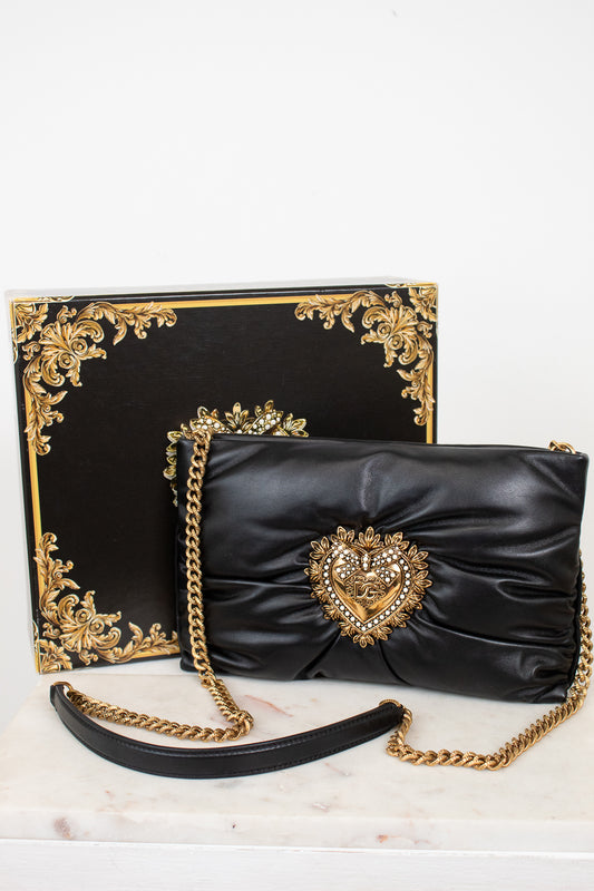 Black clutch bag with gold chain and decorative heart emblem on a white background