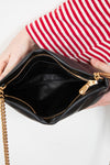 Black handbag with gold chain held by a person wearing a red and white striped shirt.