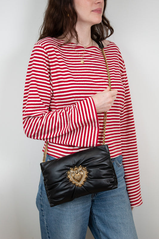 Person wearing a red and white striped shirt with a black handbag featuring a gold emblem.