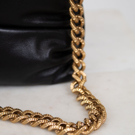 Gold chain on a black leather bag with a white background