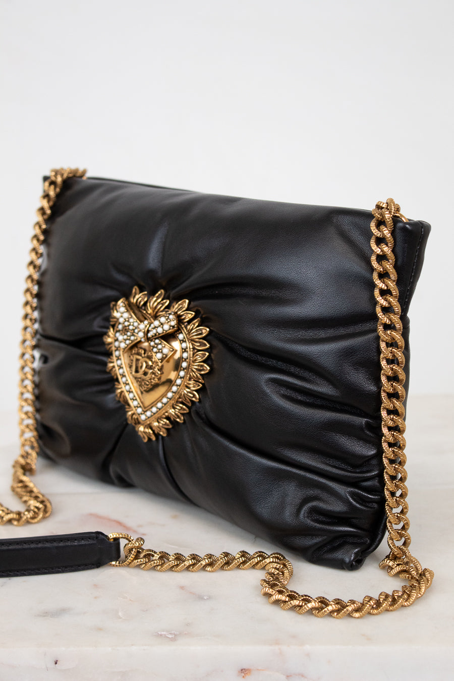 Black handbag with gold chain strap and decorative emblem on a marble surface