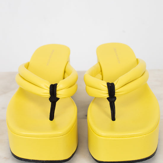 Pair of yellow sandals with black strap details on a light gray background