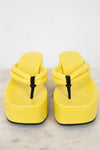Pair of yellow sandals with black strap details on a light gray background