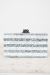 A rectangular clutch bag with horizontal stripes of silver glitter and white faux mother-of-pearl, featuring a black metal clasp with three dark beads on top, set against a white background.