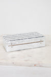 A rectangular white resin jewelry box with horizontal textured silver bands on the lid and a small gold-tone metal bar on the front, displayed on a white marble surface against a white background.