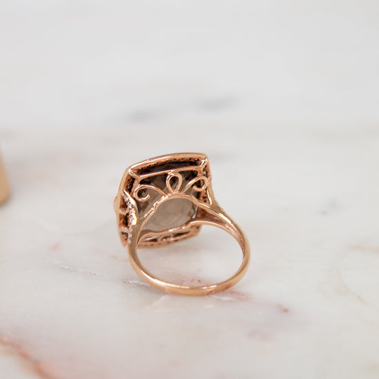 Rose gold ring with intricate design on a marble surface