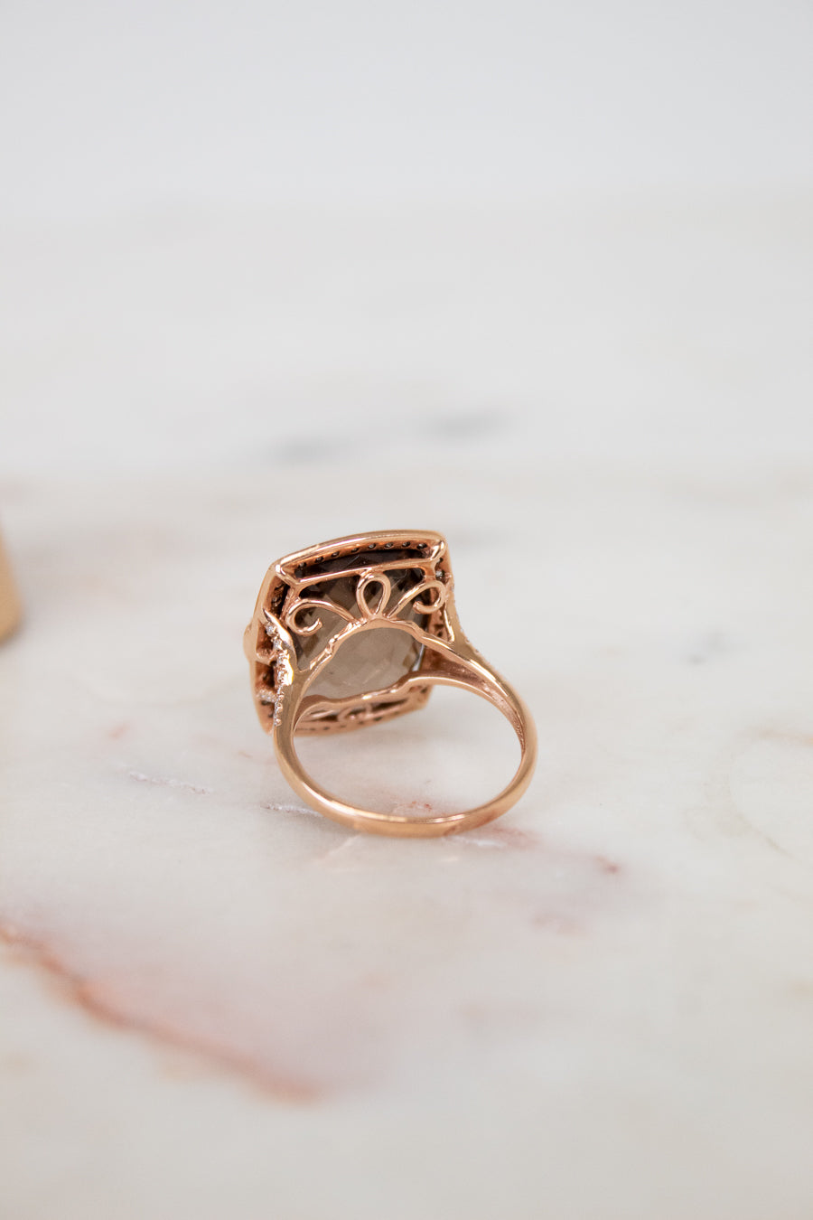 Rose gold ring with intricate design on a marble surface