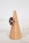 Ring with a brown gemstone on a wooden cone against a light background