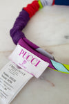 Close-up of a colorful fabric headband with a white PUCCI brand paper tag attached, resting on a light marble-like surface.