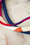 A close-up of a multi-colored fabric headband with geometric color-blocked panels in white, orange, purple, red, and navy blue, resting on a light marble surface.
