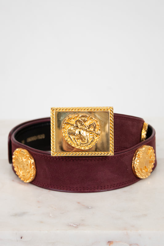 Burgundy belt with gold medallion buckle on a marble surface