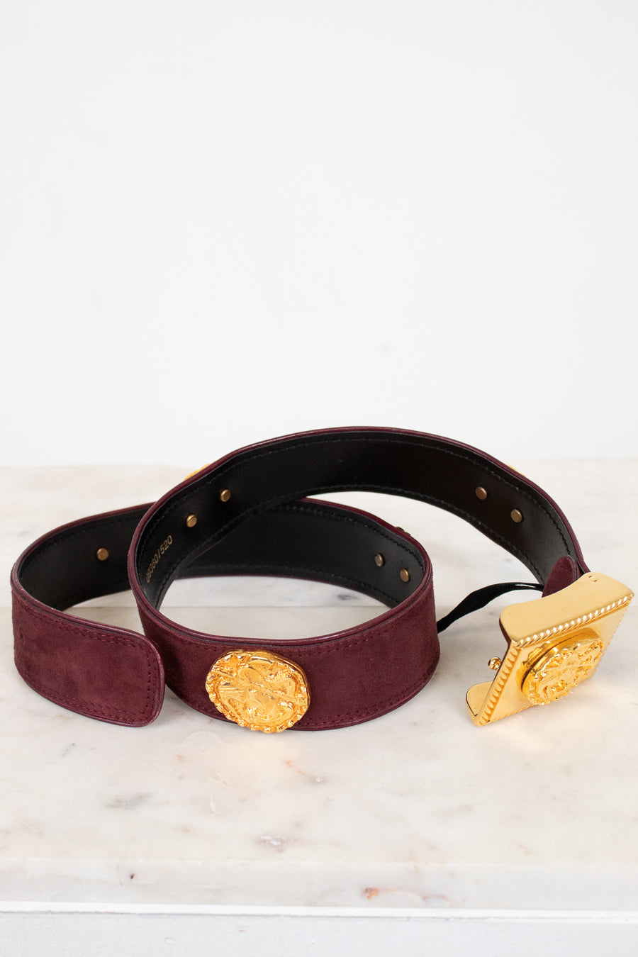 Burgundy belt with gold buckle on a light marble surface