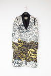 A long-sleeved floral coat with a black shawl collar, featuring a black and white floral pattern on the upper half and a black, yellow, and white floral pattern on the lower half, hanging on a white hanger against a white wall.