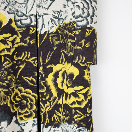 A close-up of a patterned garment, likely a kimono or robe, featuring a split design with a black and yellow floral print on the lower half and a black and gray floral print on an off-white background on the upper half.