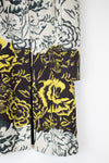 A close-up of a patterned garment, likely a kimono or robe, featuring a split design with a black and yellow floral print on the lower half and a black and gray floral print on an off-white background on the upper half.