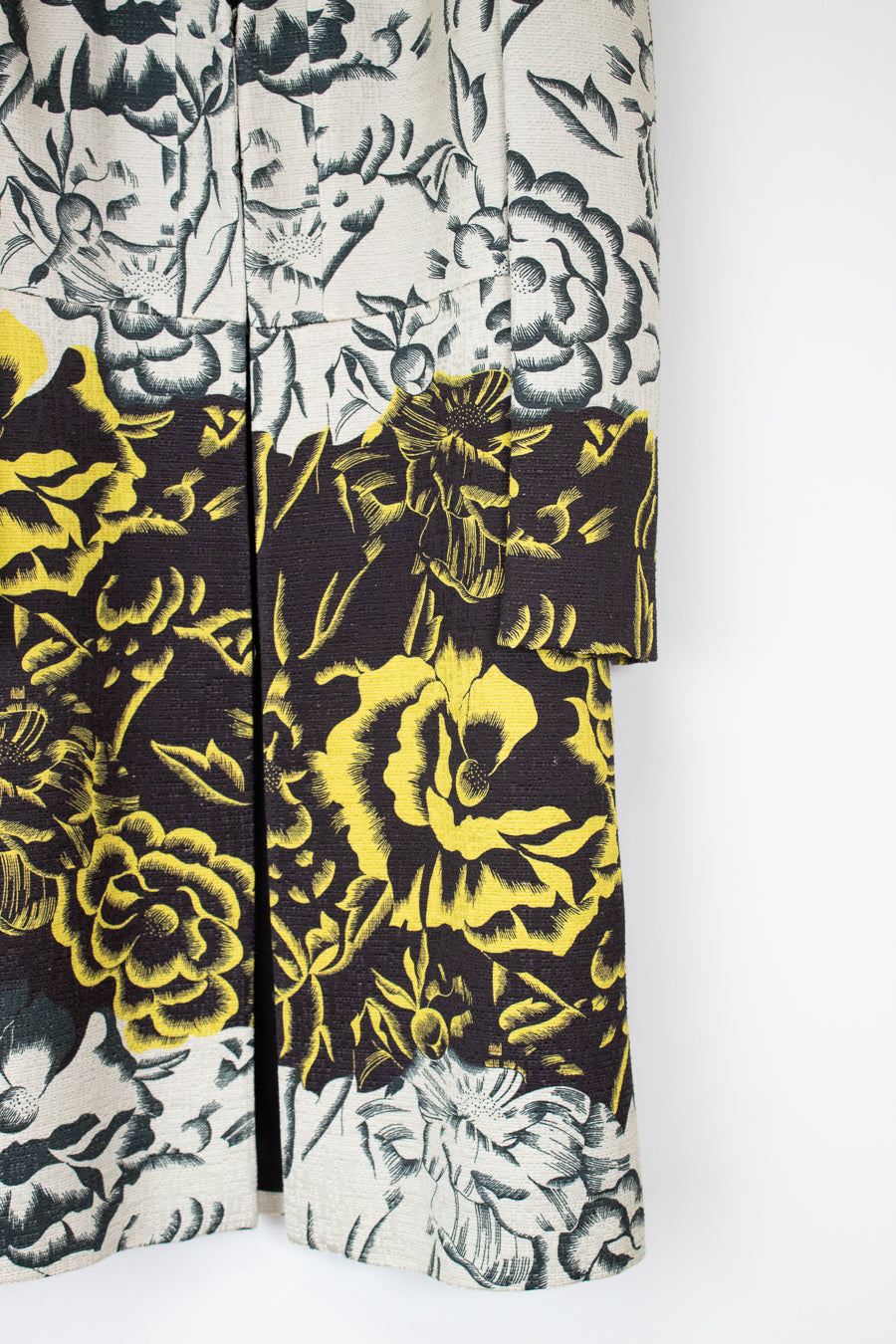 A close-up of a patterned garment, likely a kimono or robe, featuring a split design with a black and yellow floral print on the lower half and a black and gray floral print on an off-white background on the upper half.