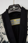 A close-up of an ETRO Milano garment hanging on a black hanger with the ETRO Milano logo. The garment has a black shawl collar and inner lining, with a patterned off-white and black outer fabric visible on the sides.