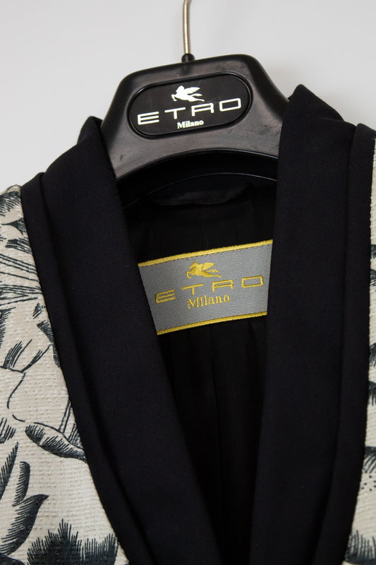 A close-up of an ETRO Milano garment hanging on a black hanger with the ETRO Milano logo. The garment has a black shawl collar and inner lining, with a patterned off-white and black outer fabric visible on the sides.