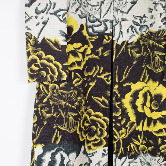 A close-up of a floral-patterned garment, likely a kimono or cardigan, featuring a split design with a black and gray floral print on the top and a black, gray, and bright yellow floral print on the bottom.