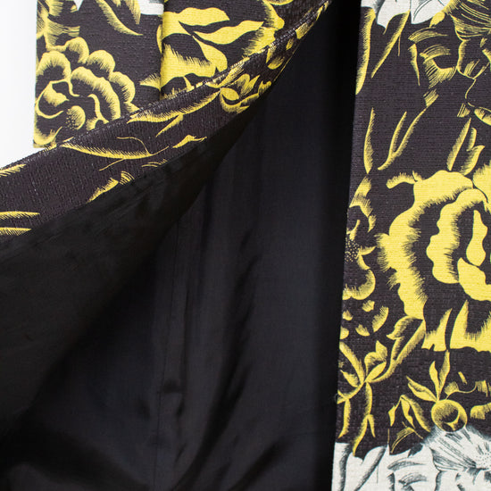Close-up of a patterned kimono-style jacket with a black satin lining, featuring a bold yellow and black floral print on a white background.