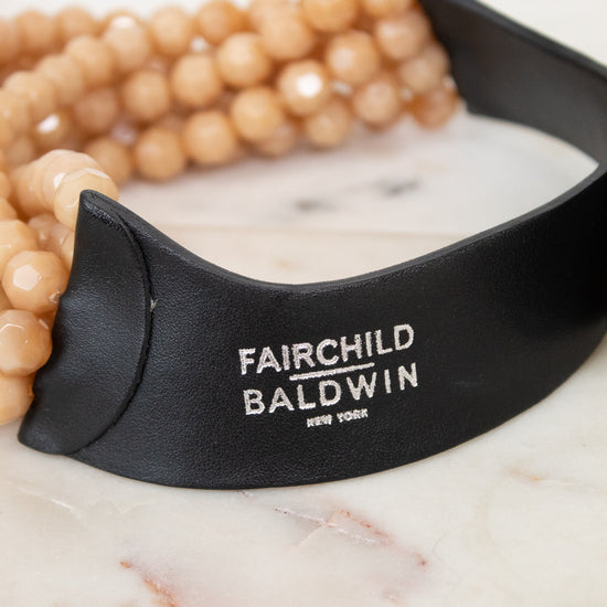Close-up of black leather closure with 'Fairchild Baldwin New York' silver logo stamping displayed against a marble background