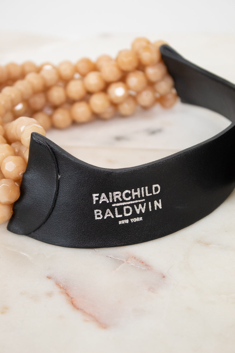 Close-up of black leather closure with 'Fairchild Baldwin New York' silver logo stamping displayed against a marble background