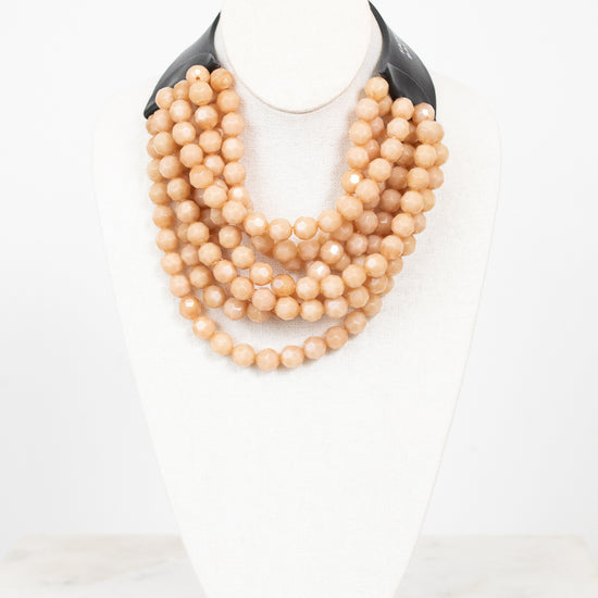Black leather with beige layered bead necklace displayed on plain bust and on a marble surface
