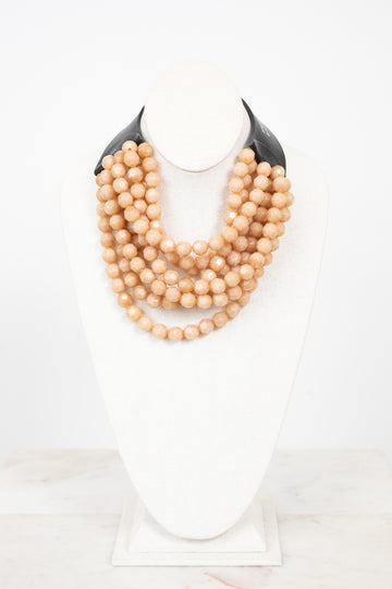 Black leather with beige layered bead necklace displayed on plain bust and on a marble surface