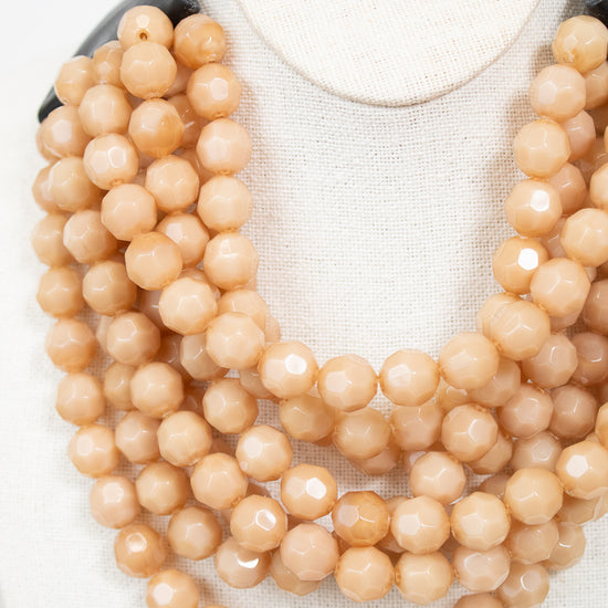 Close-up of beige layered beaded necklace attached to black leather closure and displayed against a plain background