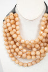 Close-up of beige layered beaded necklace attached to black leather closure and displayed against a plain background