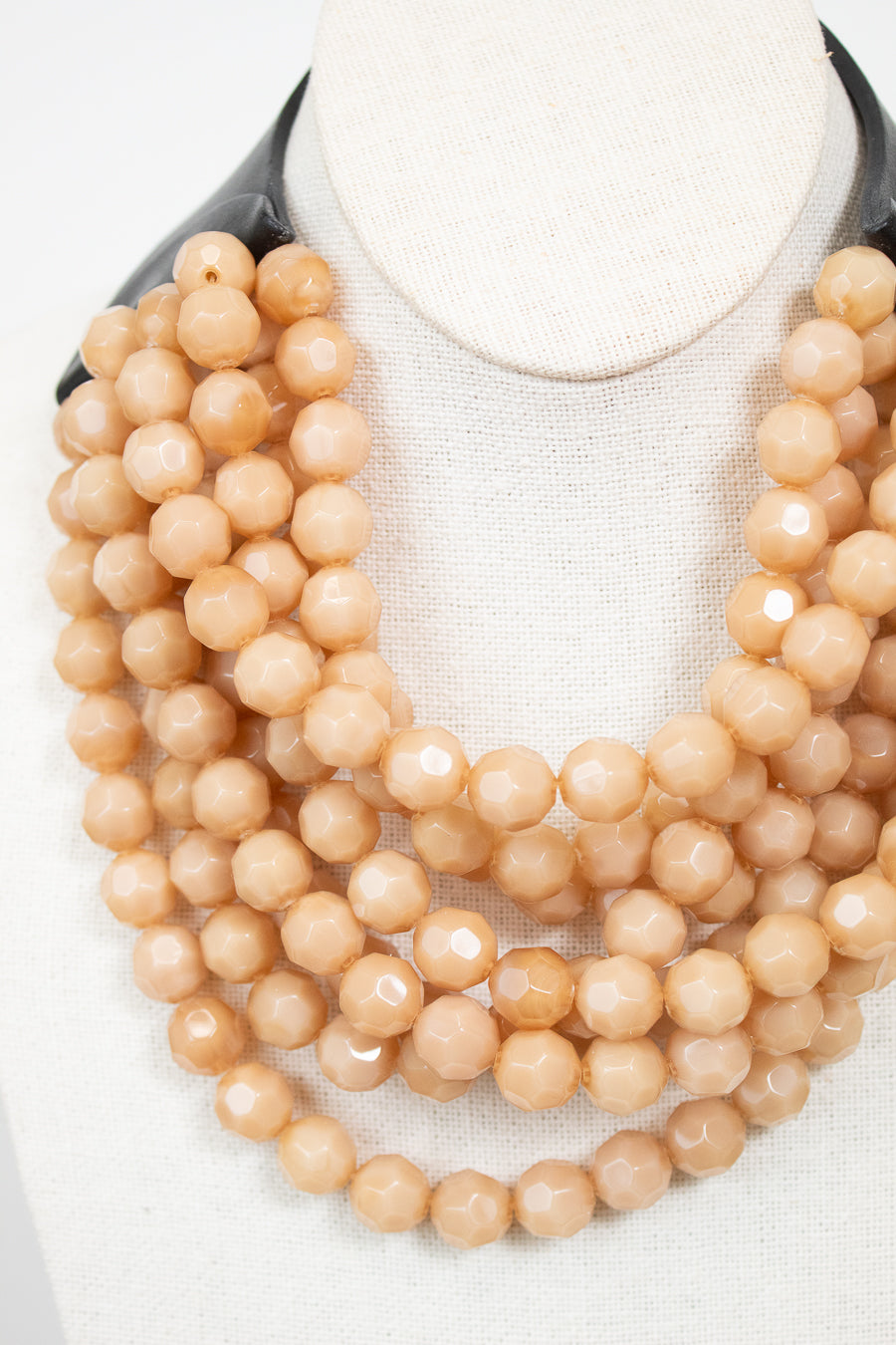 Close-up of beige layered beaded necklace attached to black leather closure and displayed against a plain background