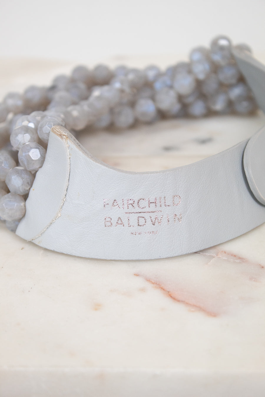 Close-up of 'Fairchild Baldwin Ney York' faded branding stamp on gray leather section displayed on top of a marble slab