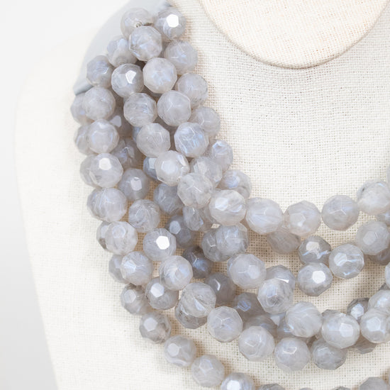 Close-up of gray layered beaded necklace displayed on plain bust