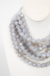 Close-up of gray layered beaded necklace displayed on plain bust