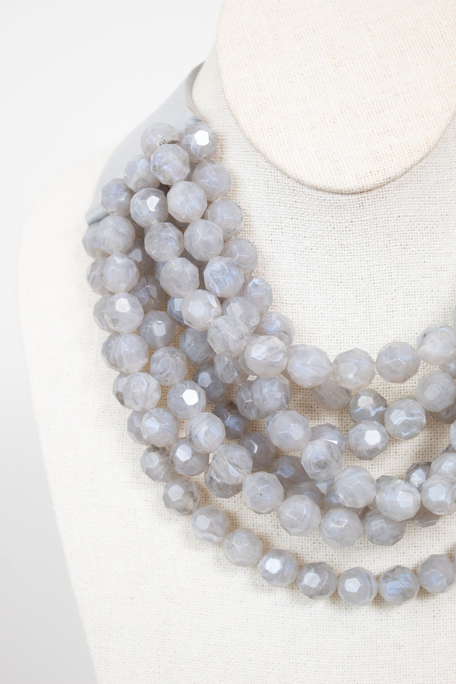 Close-up of gray layered beaded necklace displayed on plain bust