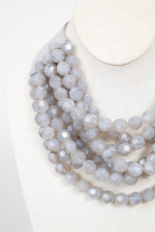 Close-up of gray layered beaded necklace displayed on plain bust