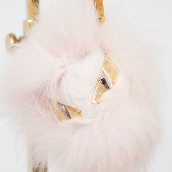 A fluffy pale pink faux-fur keychain or bag charm with gold-tone metal hardware and small geometric gold details, shown hanging against a white background.