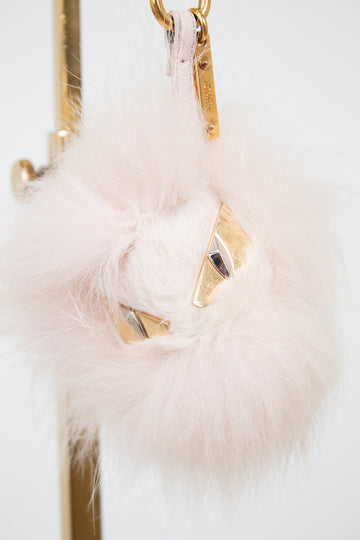A fluffy pale pink faux-fur keychain or bag charm with gold-tone metal hardware and small geometric gold details, shown hanging against a white background.