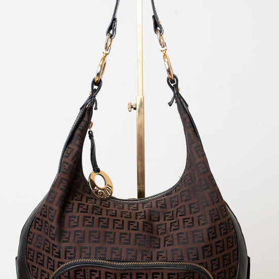 A Fendi brown monogram hobo handbag with black leather trim and gold-tone hardware, displayed on a white mannequin stand against a white background.