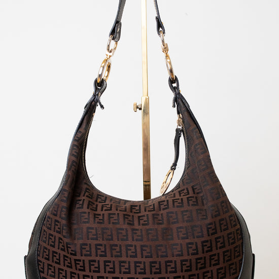 A brown Fendi hobo bag with the signature FF monogram pattern, displayed on a gold stand against a white background.