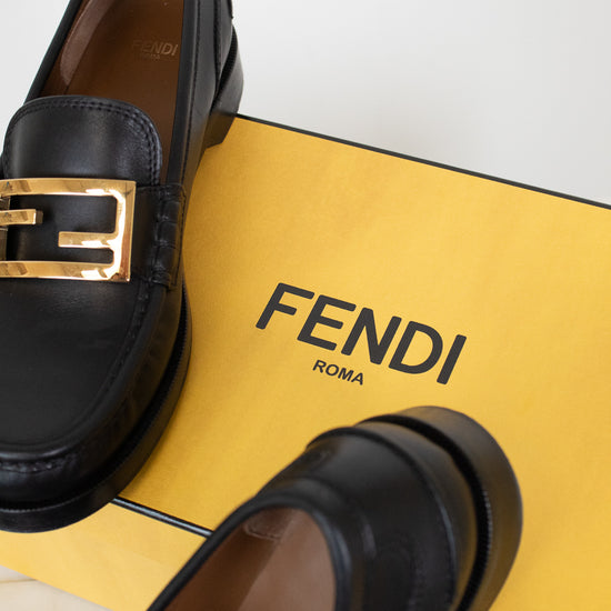 Black loafers with gold logo on a yellow Fendi branded box