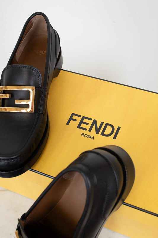 Black loafers with gold logo on a yellow Fendi branded box