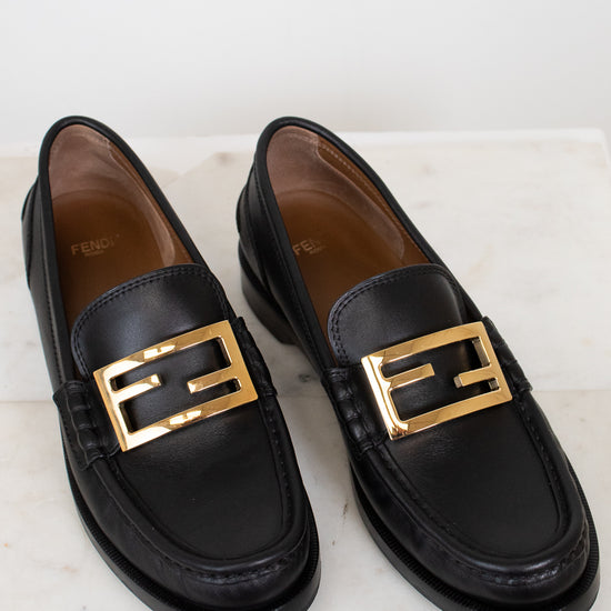 Black loafers with gold buckles on a light background