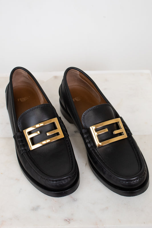 Black loafers with gold buckles on a light background