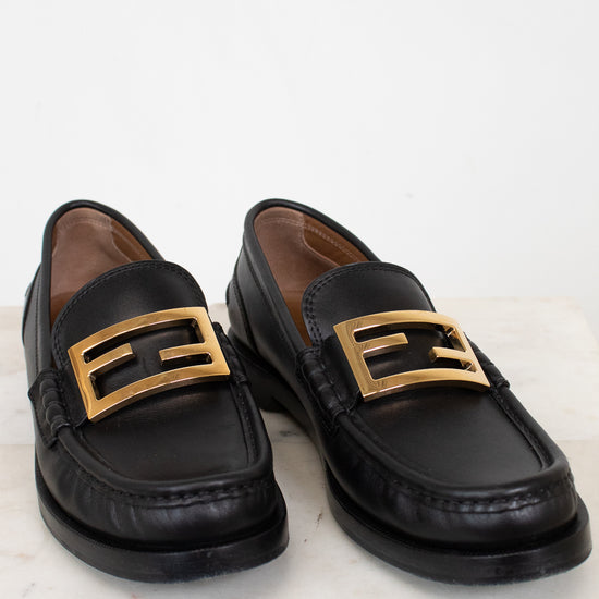Black loafers with gold buckles on a white marble surface