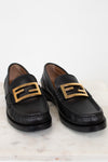 Black loafers with gold buckles on a white marble surface