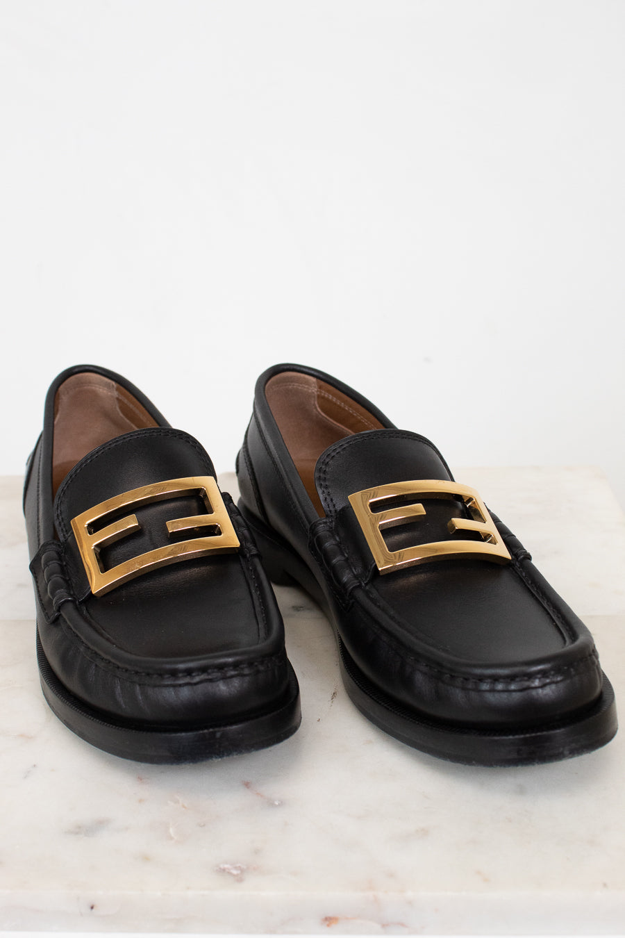 Black loafers with gold buckles on a white marble surface